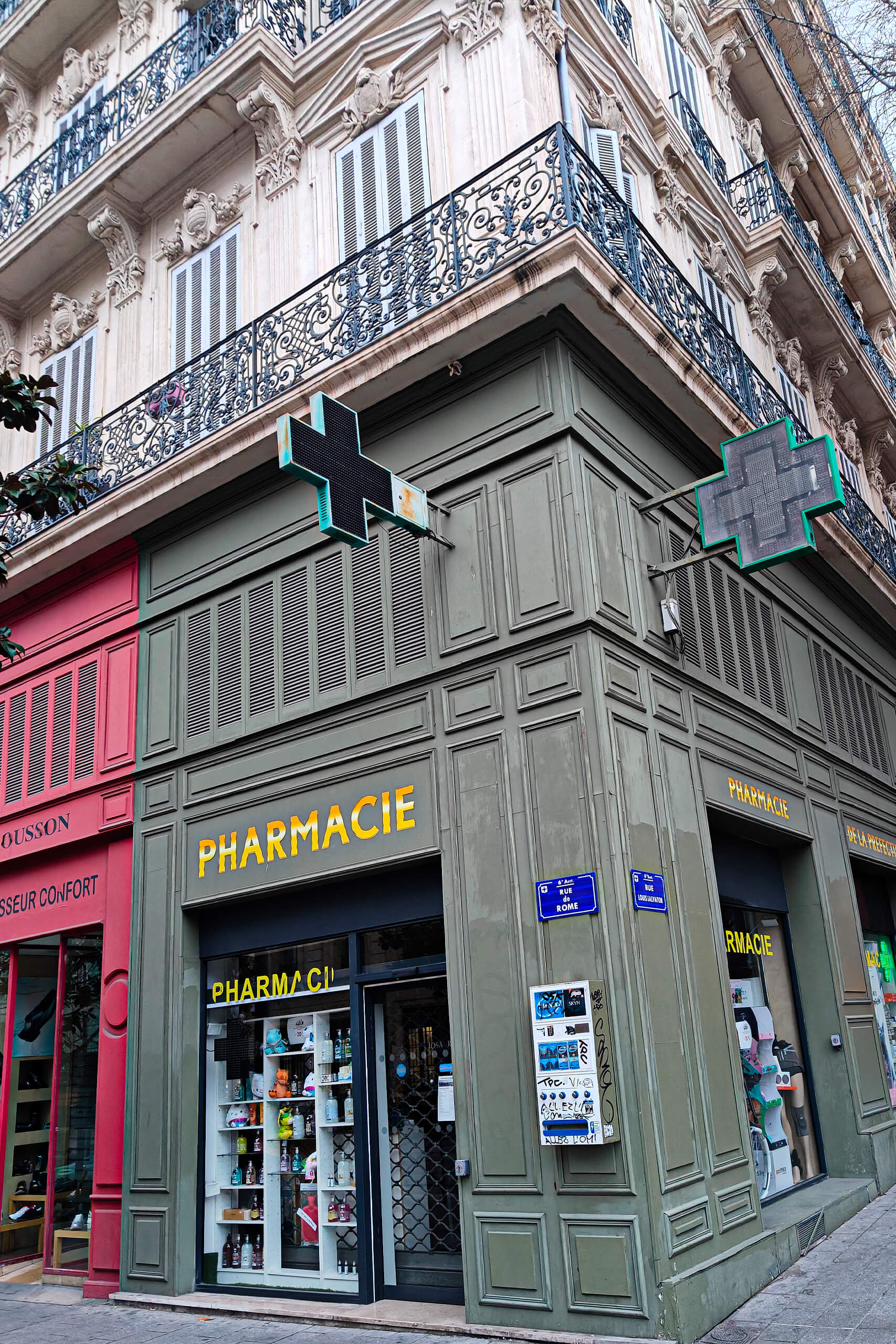 French pharmacy storefront with green cross sign on a Haussmann building